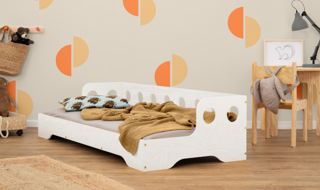 Drewniane łóżko z barierką o okrągłych wycięciach na długim boku wykonane ze sklejki sosnowej w kolorze białym